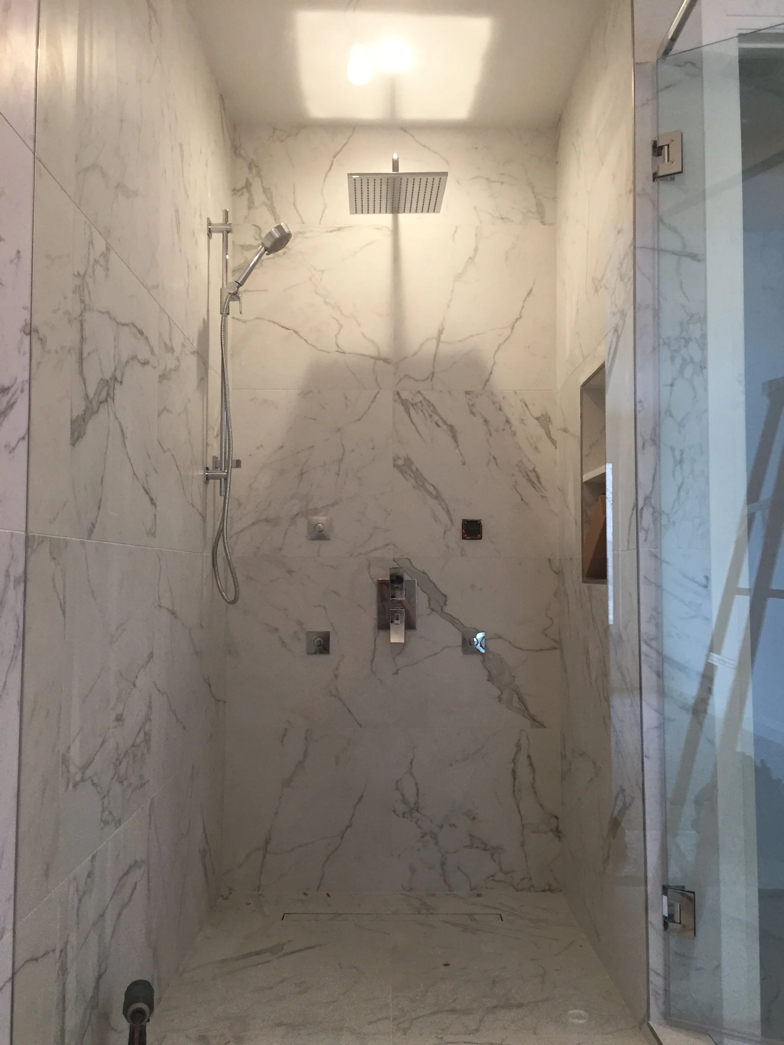Empty walk-in shower with marble walls, a rain showerhead, a handheld showerhead, and built-in shelves.
