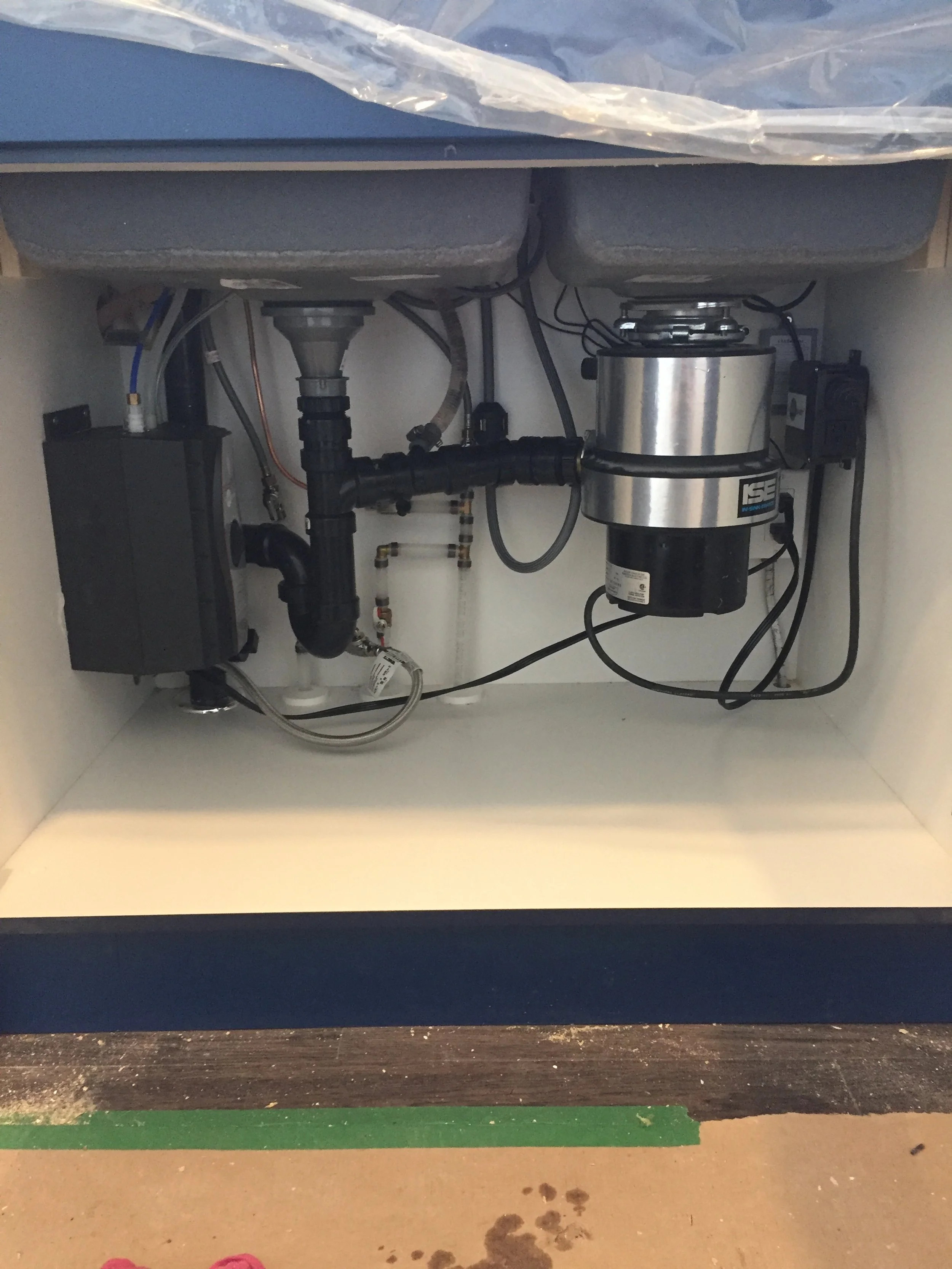Under-sink view showing plumbing and a small water filtration or pump system.