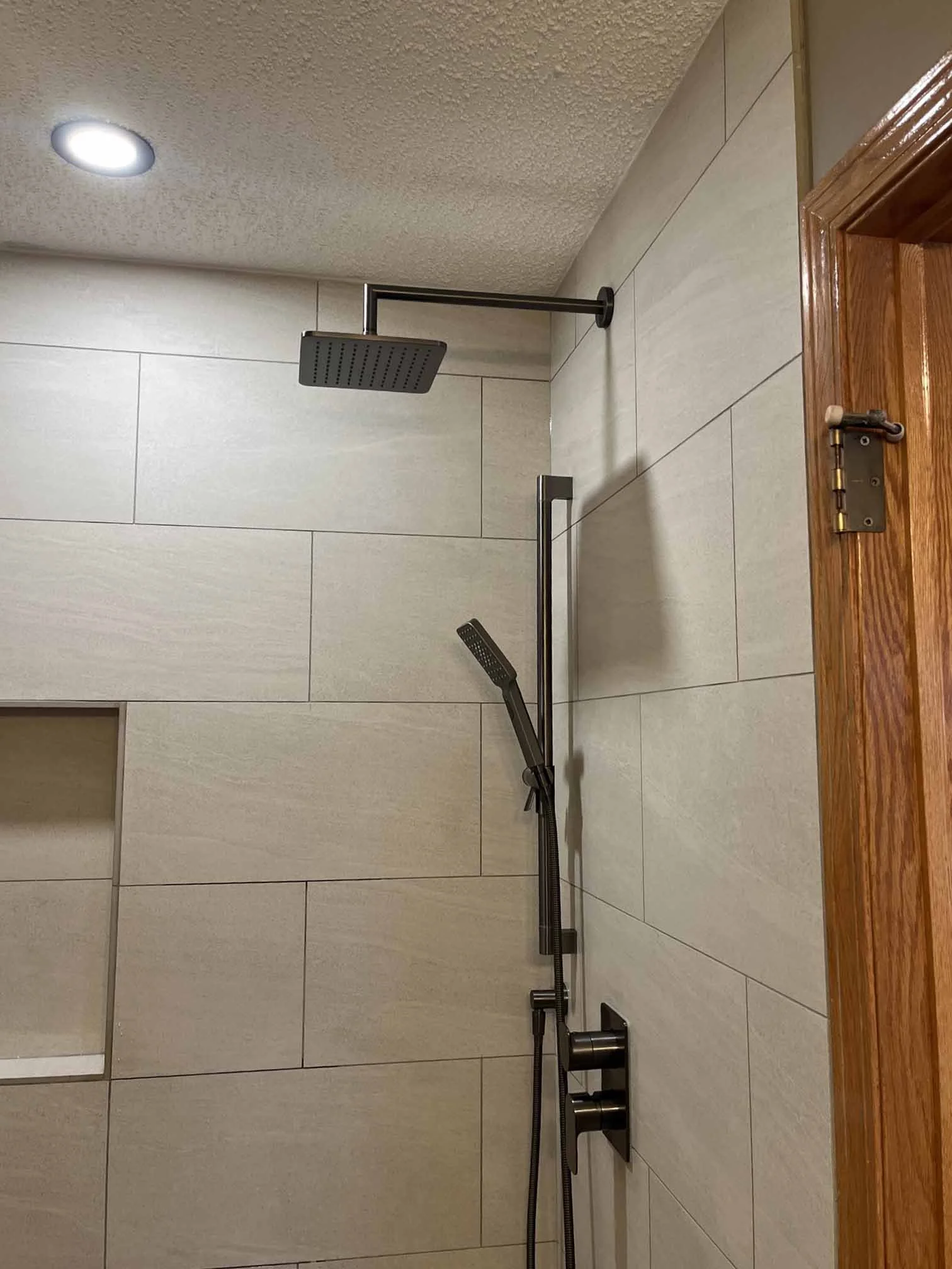 Modern shower with a large rain showerhead, a handheld showerhead on a sliding bar, and a built-in wall niche in a bathroom with beige tiles.