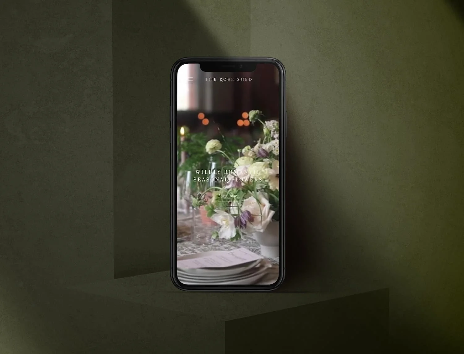 iPhone mockup displaying The Rose Shed florist mobile website featuring wildly romantic seasonal flowers on a dark background