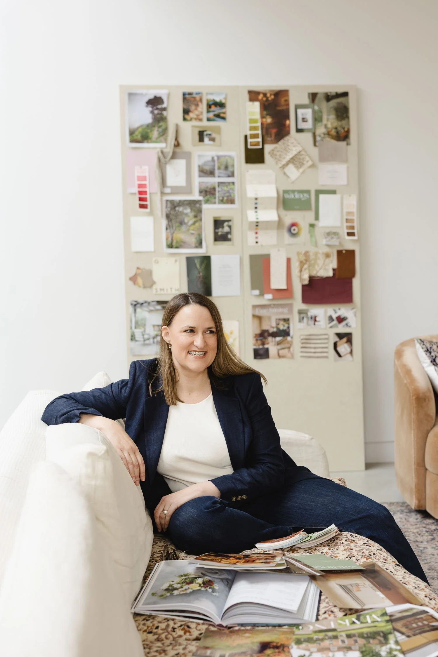 A smiling female designer sitting on a sofa in front of a large wall-mounted mood board filled with fabric and colour swatches
