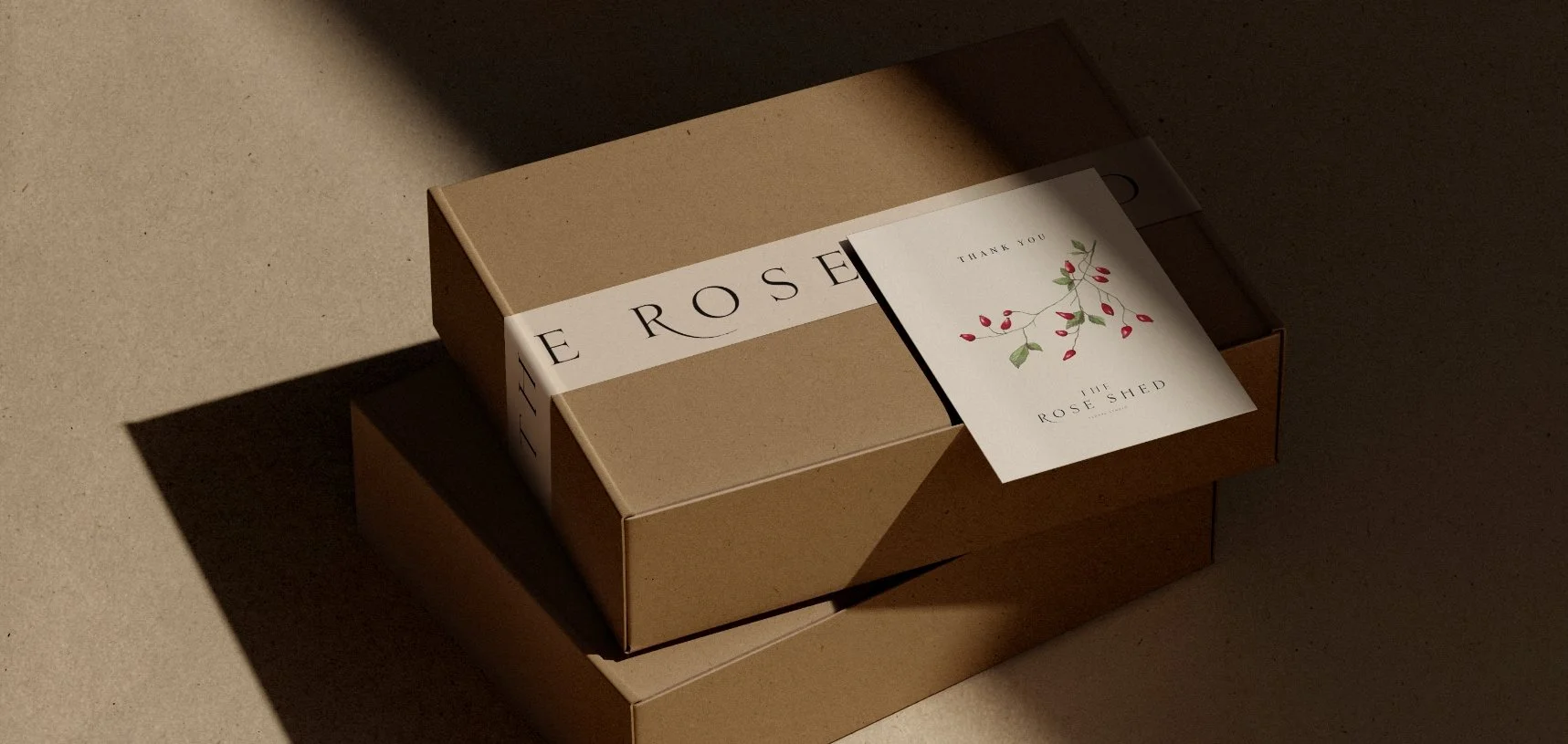 Two cardboard delivery boxes with a branded paper band and a thank you card featuring a botanical rose hip illustration