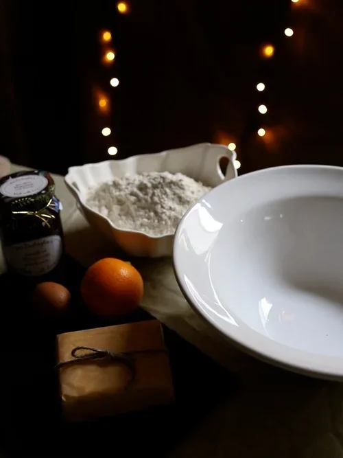 Ingredients for mince pies including a jar of mincemeat an egg an orange and butter arranged on a table with a bowl