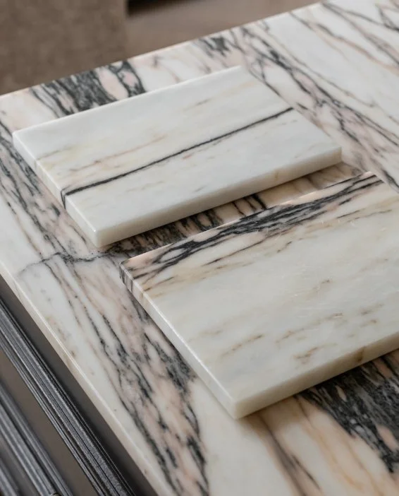 Two rectangular white marble samples with grey veining resting on a matching large stone surface in an interior studio