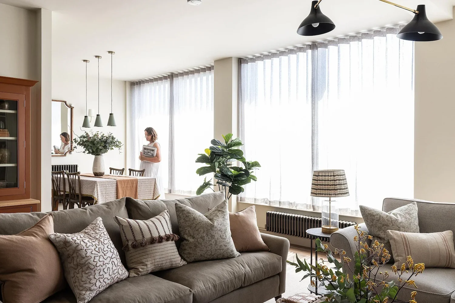 A luxury Yorkshire living room interior styled with a neutral sofa, patterned cushions, sheer curtains and a dining area