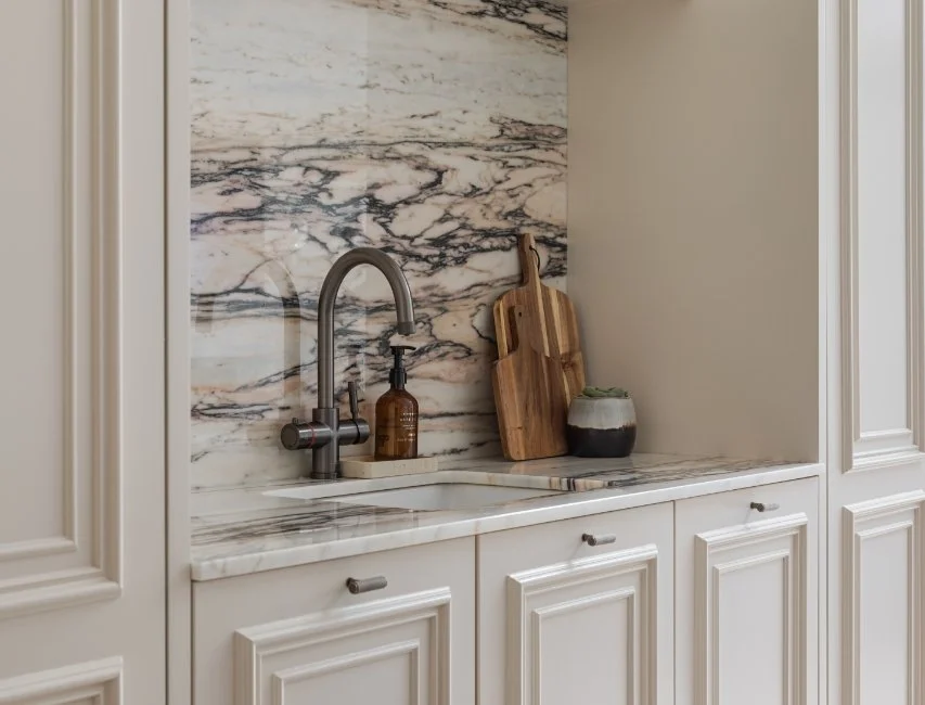 Close up of a modern kitchen sink and bronze tap with a striking marble backsplash and wooden chopping boards