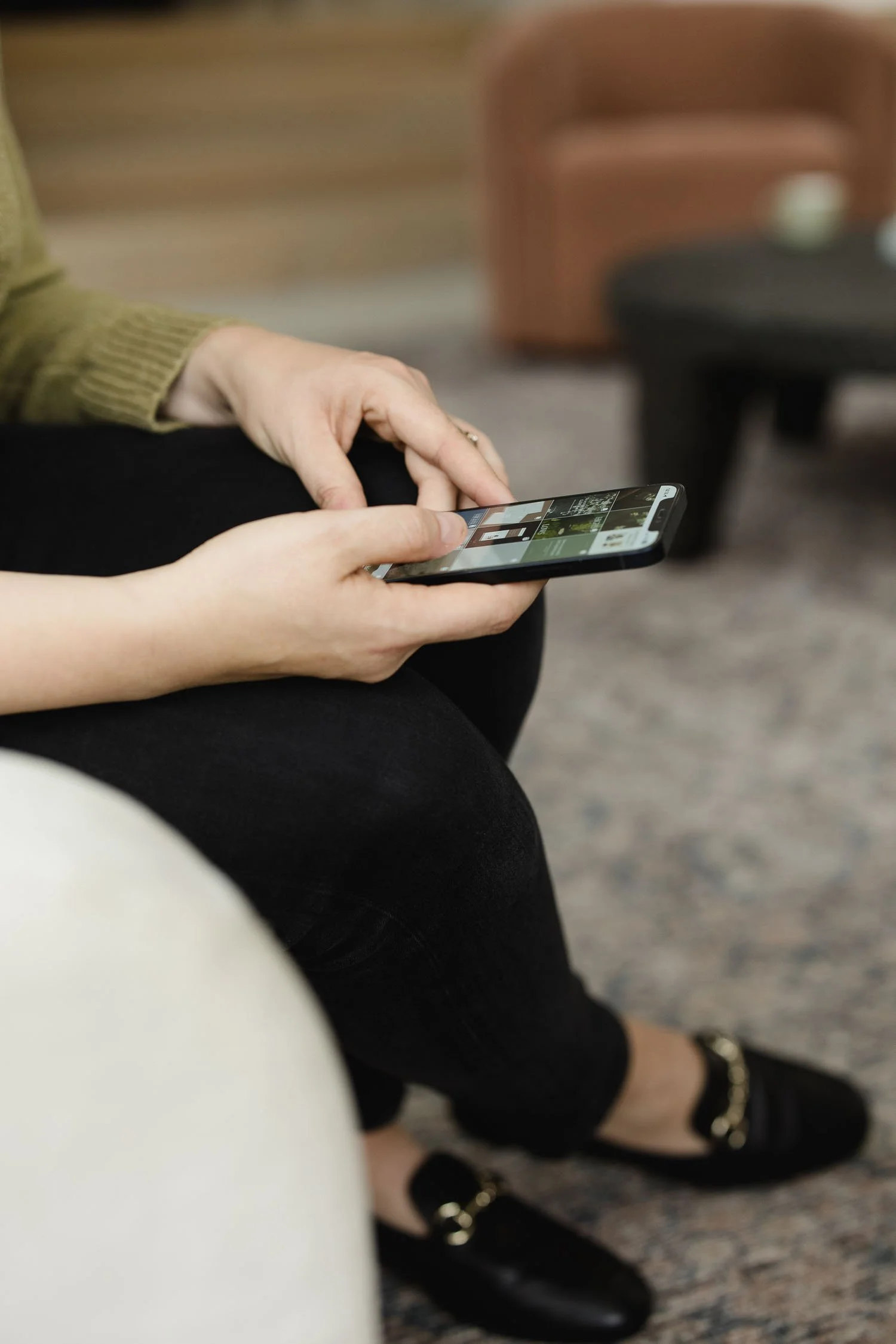 Person in a green jumper using a smartphone to scroll through a grid of professional photography and branding portfolio work