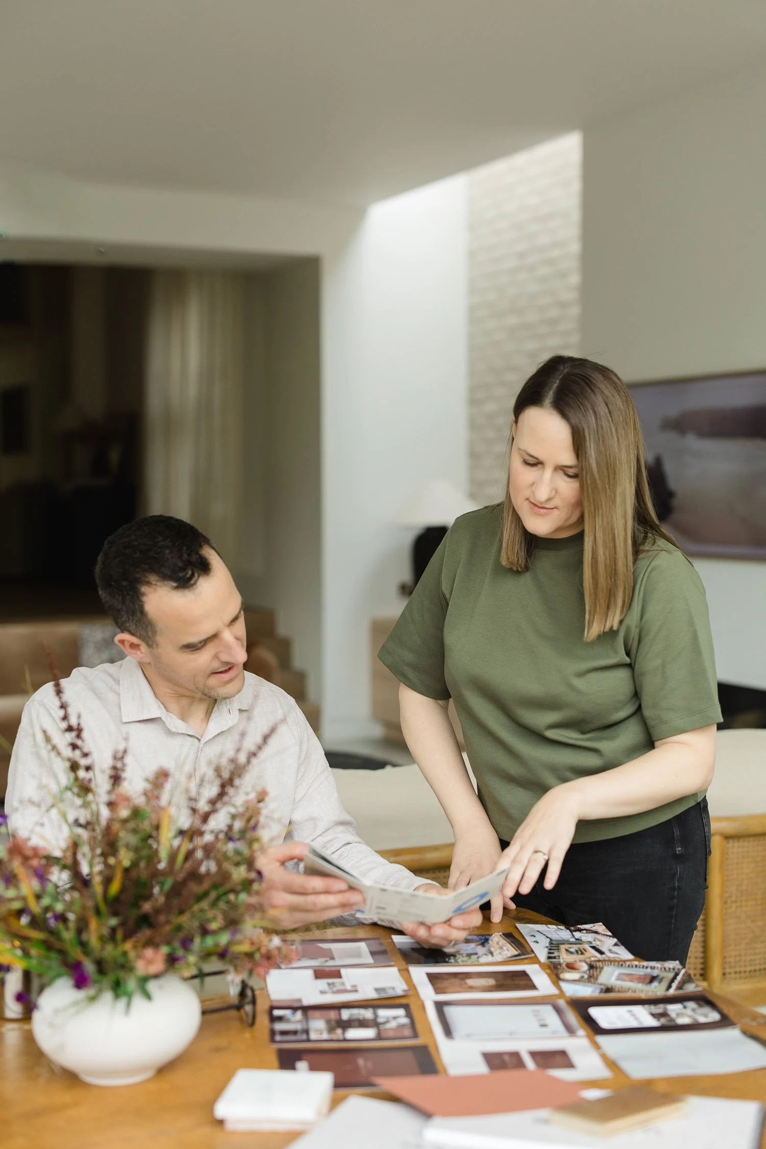 Two designers standing over a wooden table discussing printed brand strategy documents and interior design photography