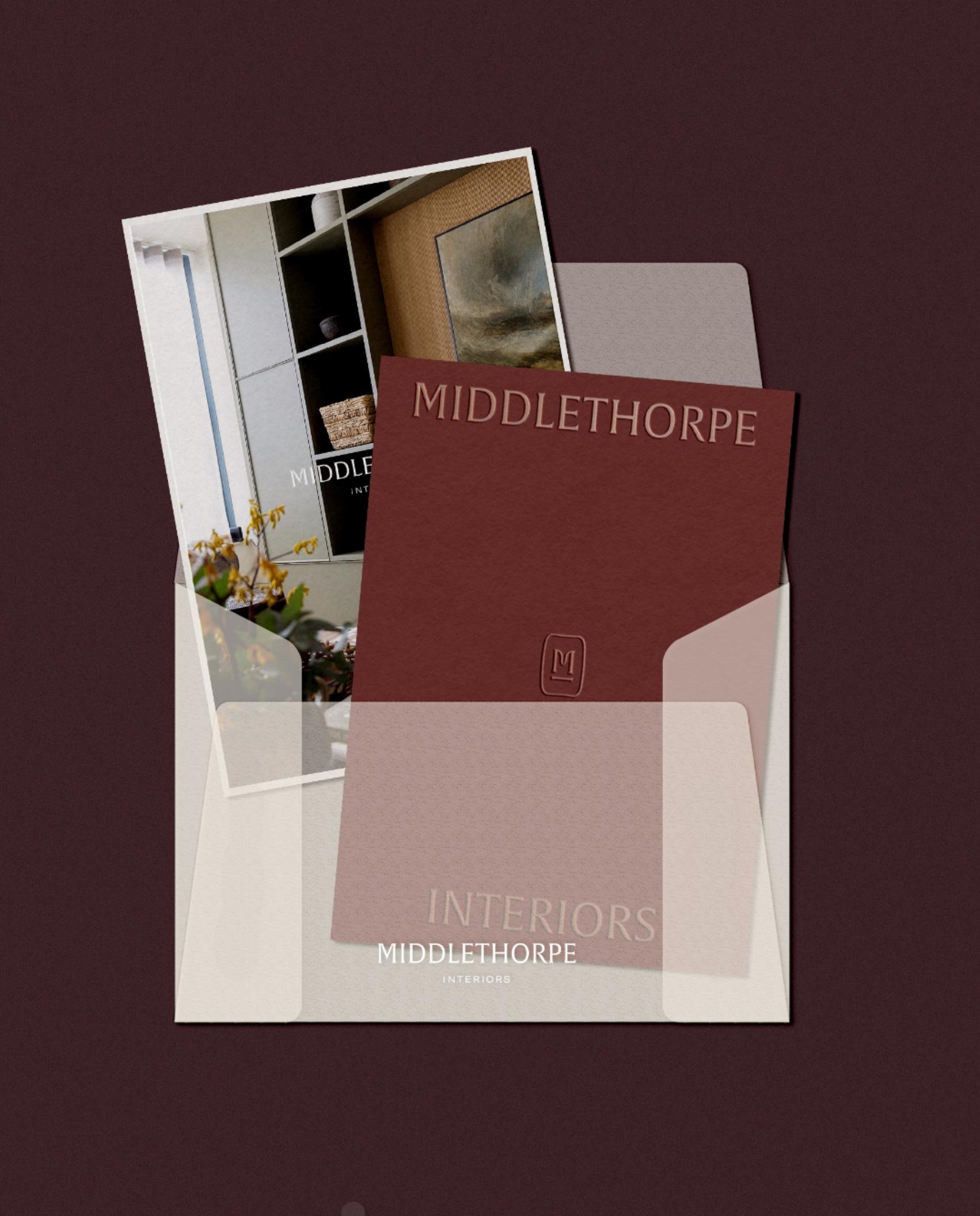 Translucent envelope containing a burgundy branded card and a high-quality photograph of a modern living room interior