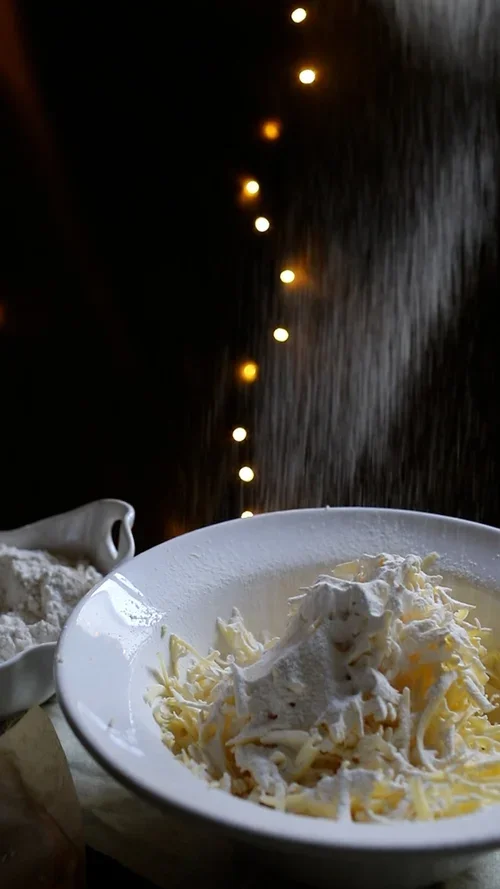 White flour being sieved over a pile of grated butter in a ceramic bowl to begin the process of making shortcrust pastry