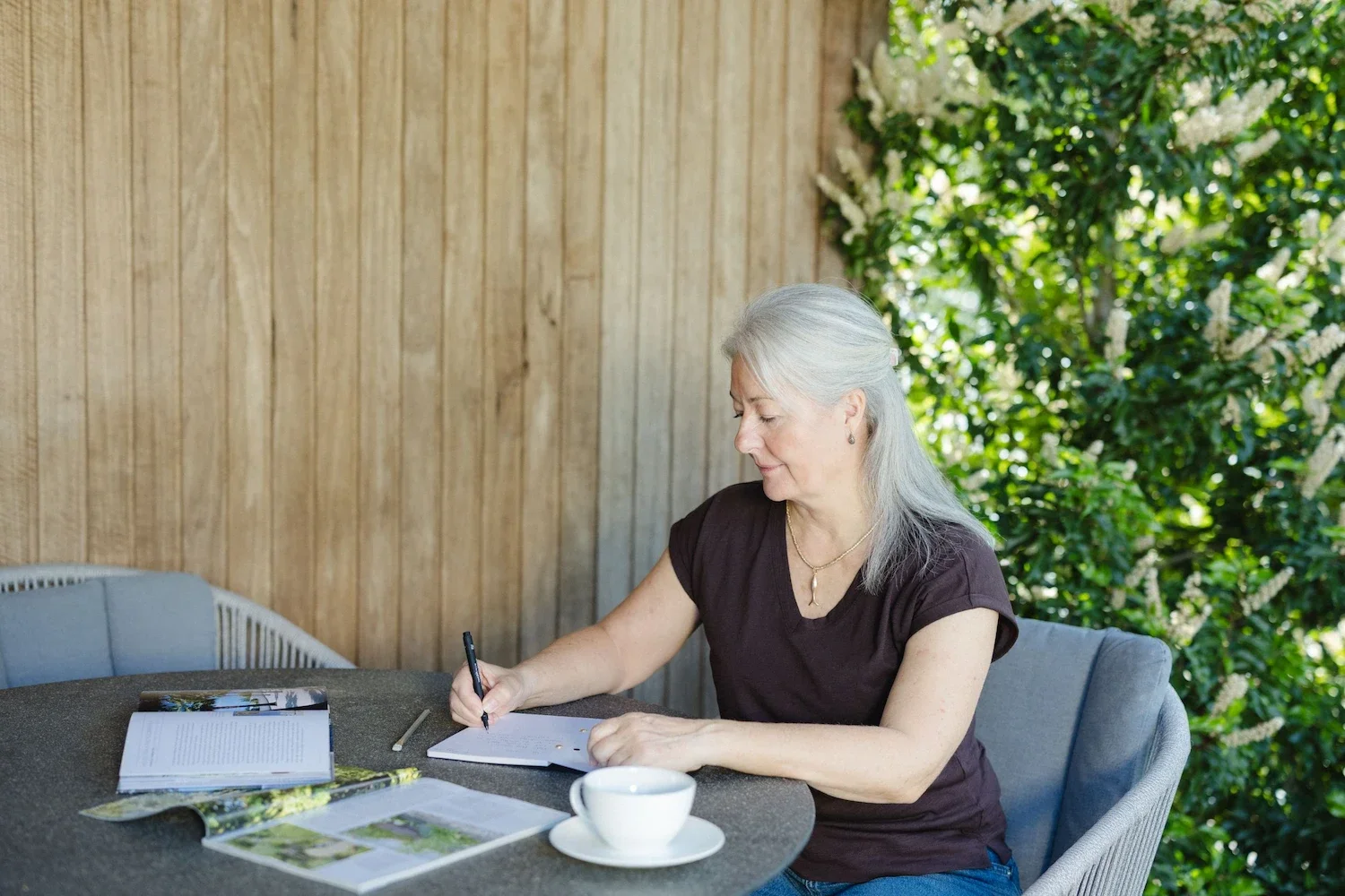Garden designer taking notes on a notepad while sitting at an outdoor patio table near lush green trees