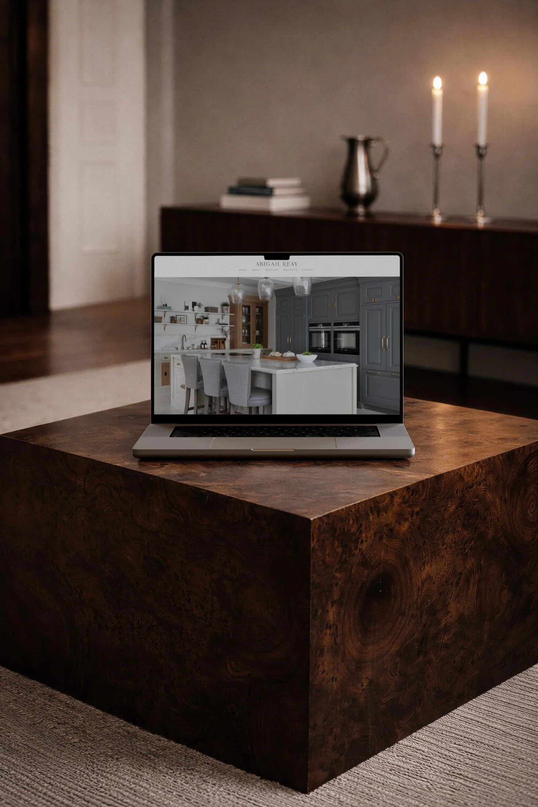 Laptop on a wooden plinth displaying a high-end interior design website with a modern kitchen portfolio for Abigail Reay
