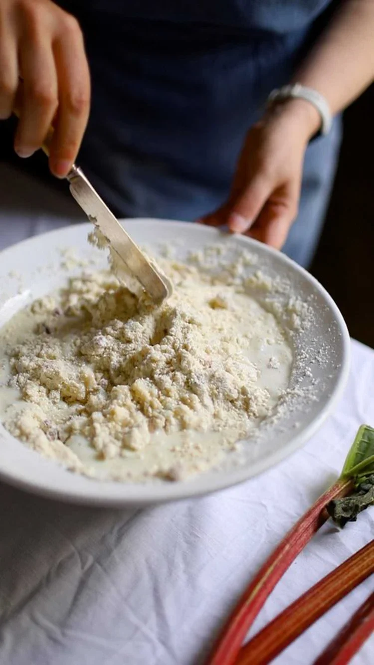Person using a butter knife to gently fold liquid into a flour mixture in a white bowl to create scone dough