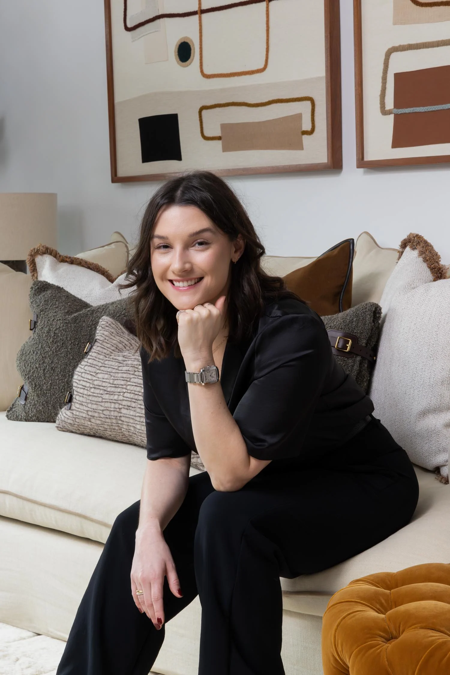 Portrait of interior designer Abigail Reay smiling on a cream sofa in a modern London studio with abstract wall art