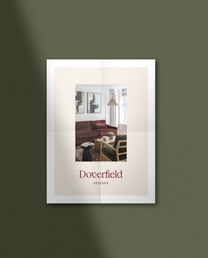 A folded brochure on a green background showing a living room with a velvet sofa wooden chair and a tall floor lamp