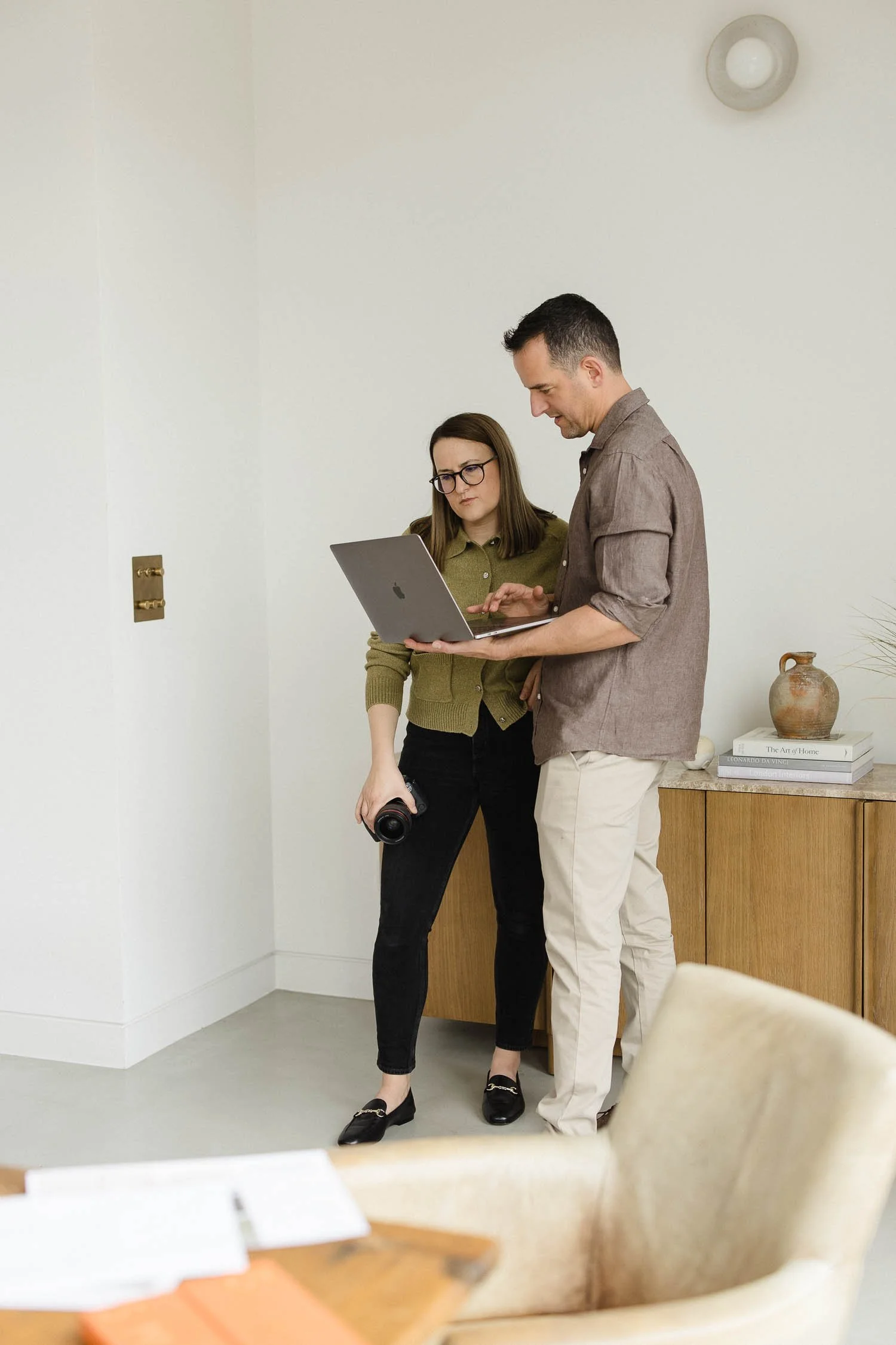 A male and female professional reviewing a website design portfolio on a laptop while holding a digital camera in a studio