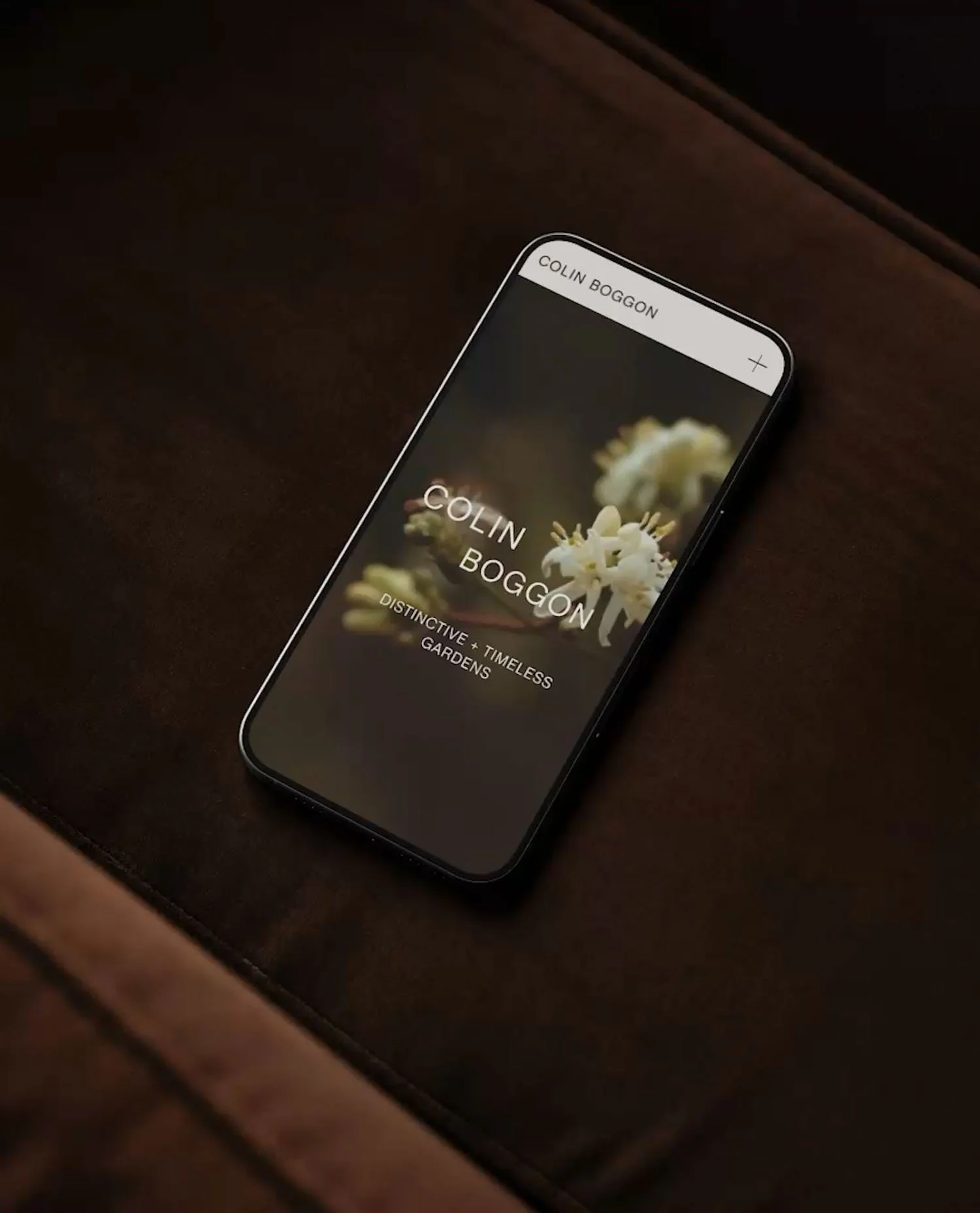 Smartphone on a brown velvet surface displaying the Colin Boggon garden design website with a dark floral hero image and text