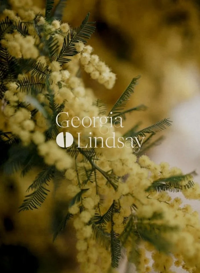 Close up of yellow mimosa blossoms with the Georgia Lindsay Landscape and Garden Design logo overlaid in a white serif font
