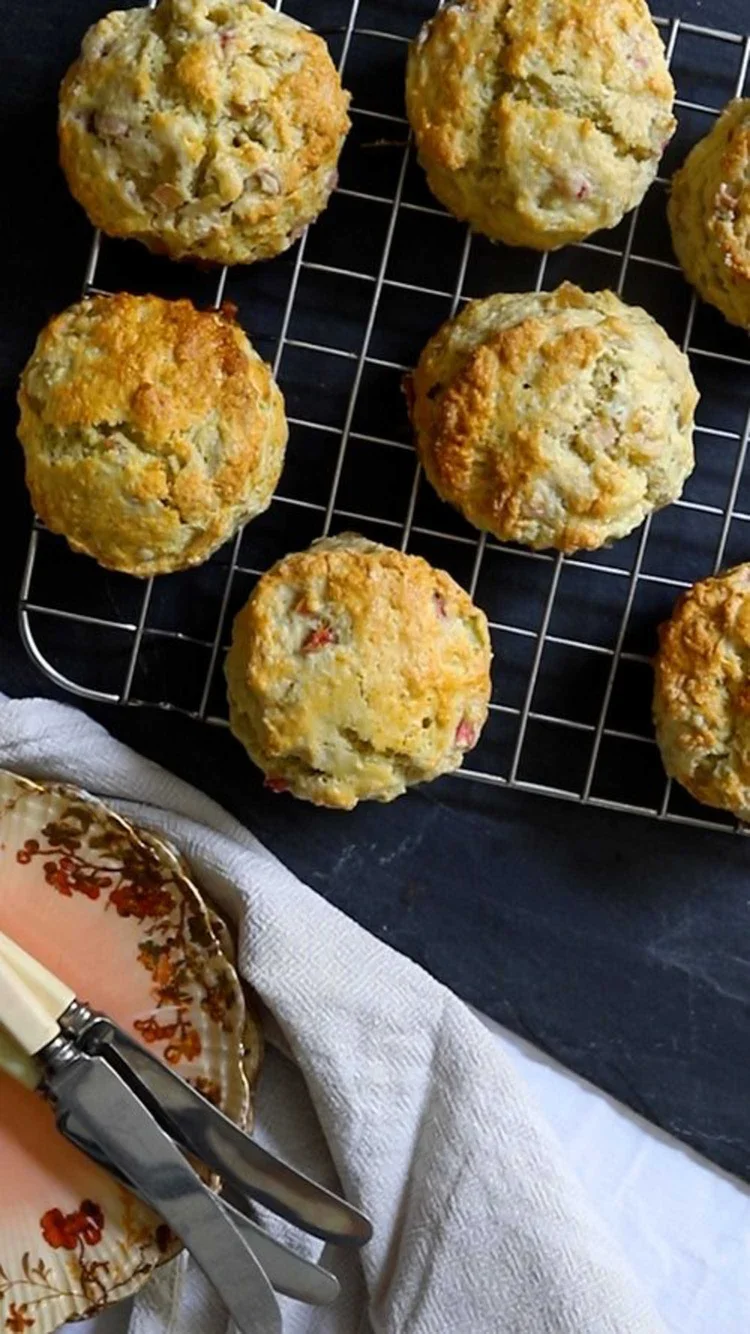 Overhead view of six freshly baked golden brown scones cooling on a wire rack next to a vintage plate and knife