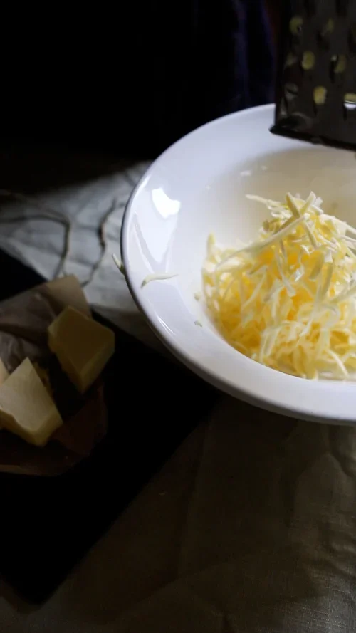 Close up of a metal grater being used to shred cold butter into a white bowl for a homemade mince pie pastry recipe