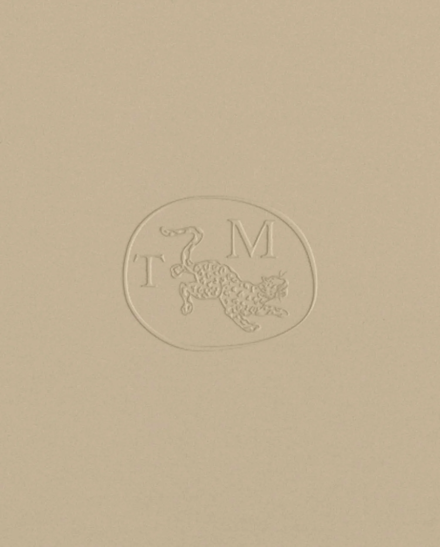 Embossed oval seal on beige paper featuring a leaping leopard between the letters T and M for an interior design brand