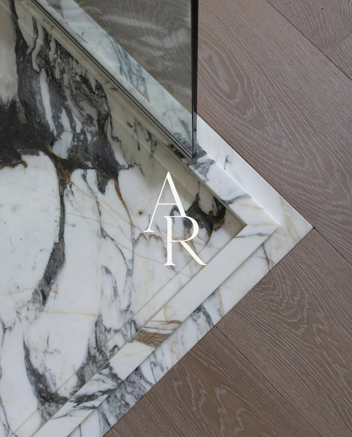 Close-up of white and grey marble flooring meeting light oak wood planks with the Abigail Reay logo for a bathroom project