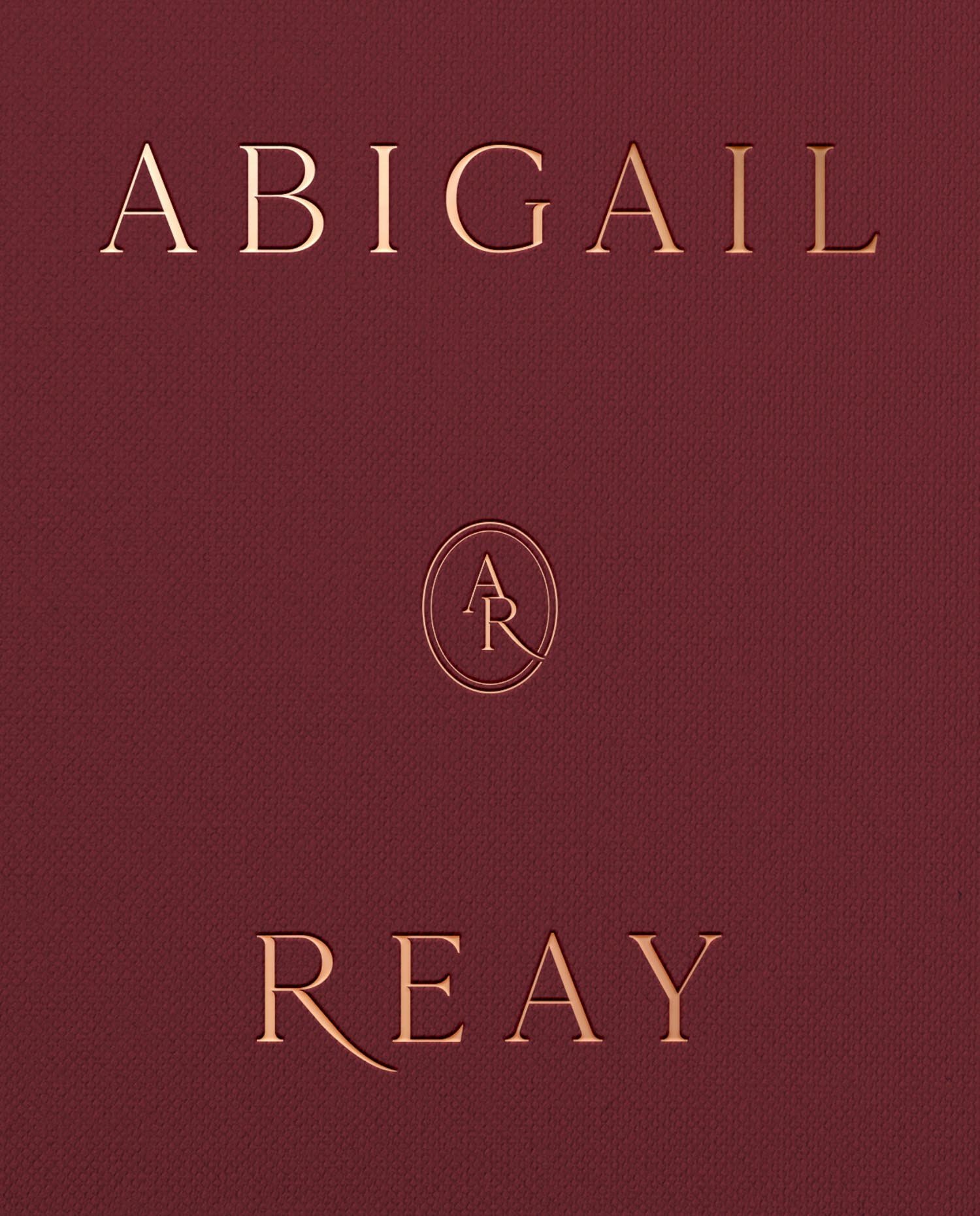 Close-up of the Abigail Reay logo and monogram embossed on a luxury deep burgundy textured paper for high-end branding