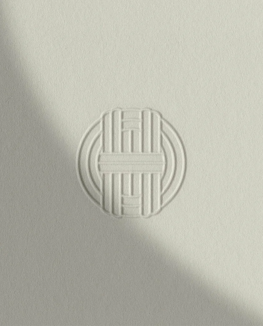Close up of an elegant embossed circular logo on textured cream paper representing the Tom Howard Garden Design brand