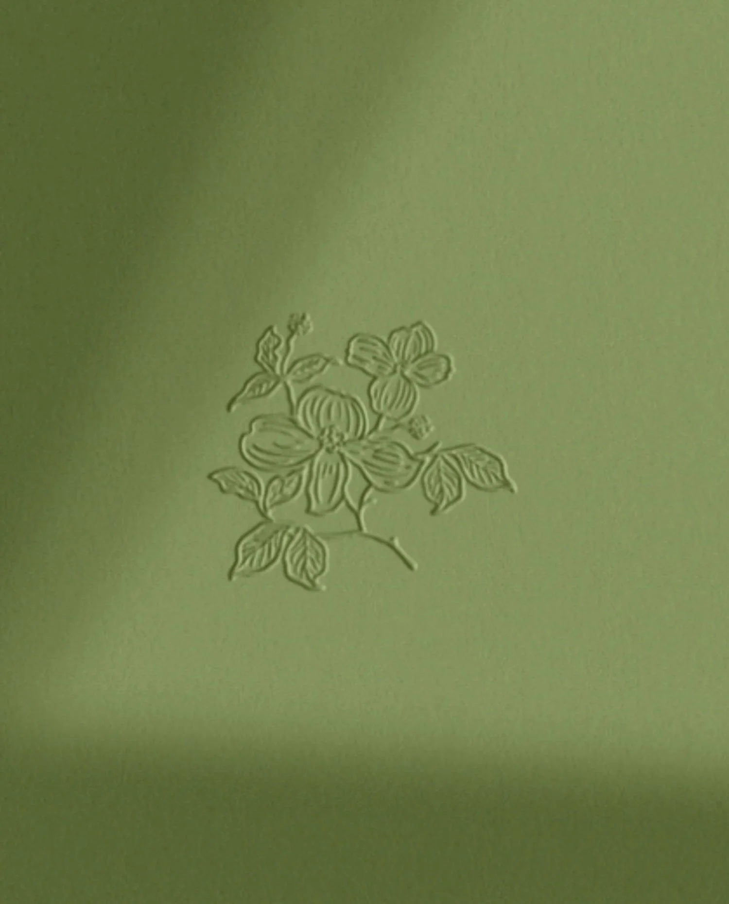 Detailed view of a single debossed floral motif on premium green textured paper reflecting high-end brand craftsmanship