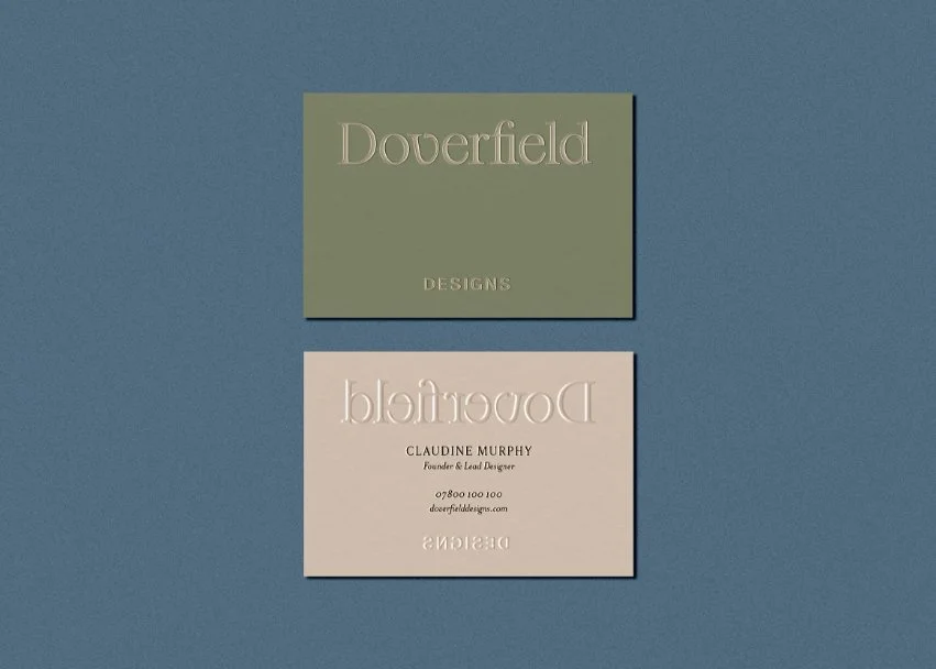 Two business cards on a blue background showing the embossed brand name on green card and contact details on beige card