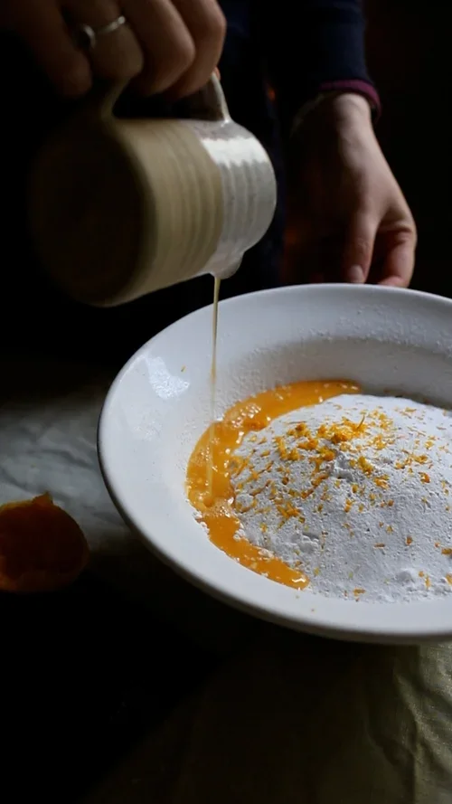 Pouring whisked egg and orange zest into a bowl of white flour to create a citrus flavoured pastry dough for mince pies