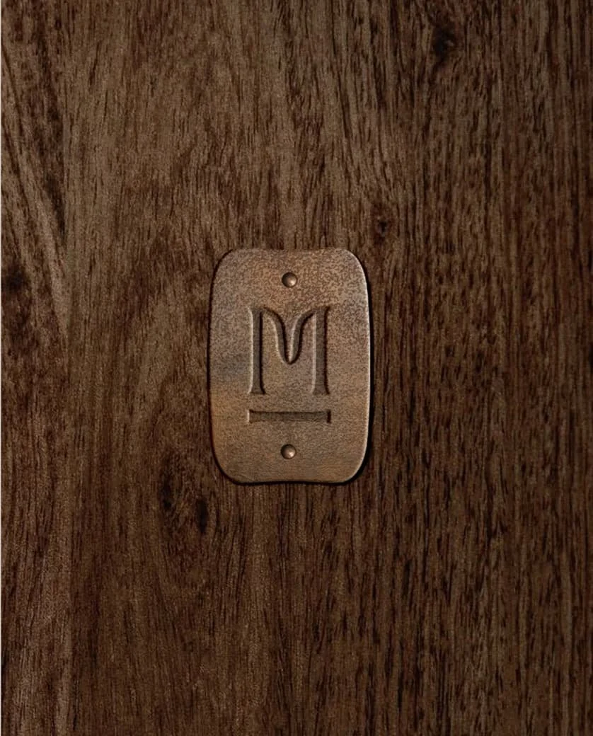 Close-up of a weathered brass logo plaque with the Middlethorpe Interiors 'M' emblem mounted on dark textured wood