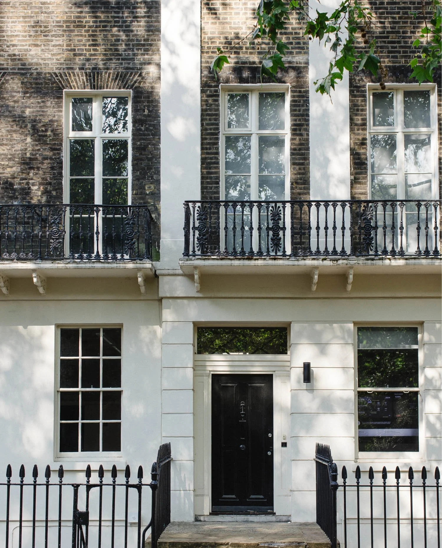 The exterior of a traditional London brick building with a black front door white window frames and ornate iron balconies