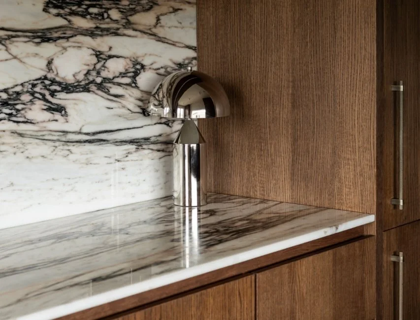 Minimalist chrome dome lamp on a white and grey veined marble surface set against a dark wood wall for a modern interior
