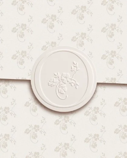 Close up of a cream circular wax seal with an embossed floral sprig design placed on matching patterned floral paper
