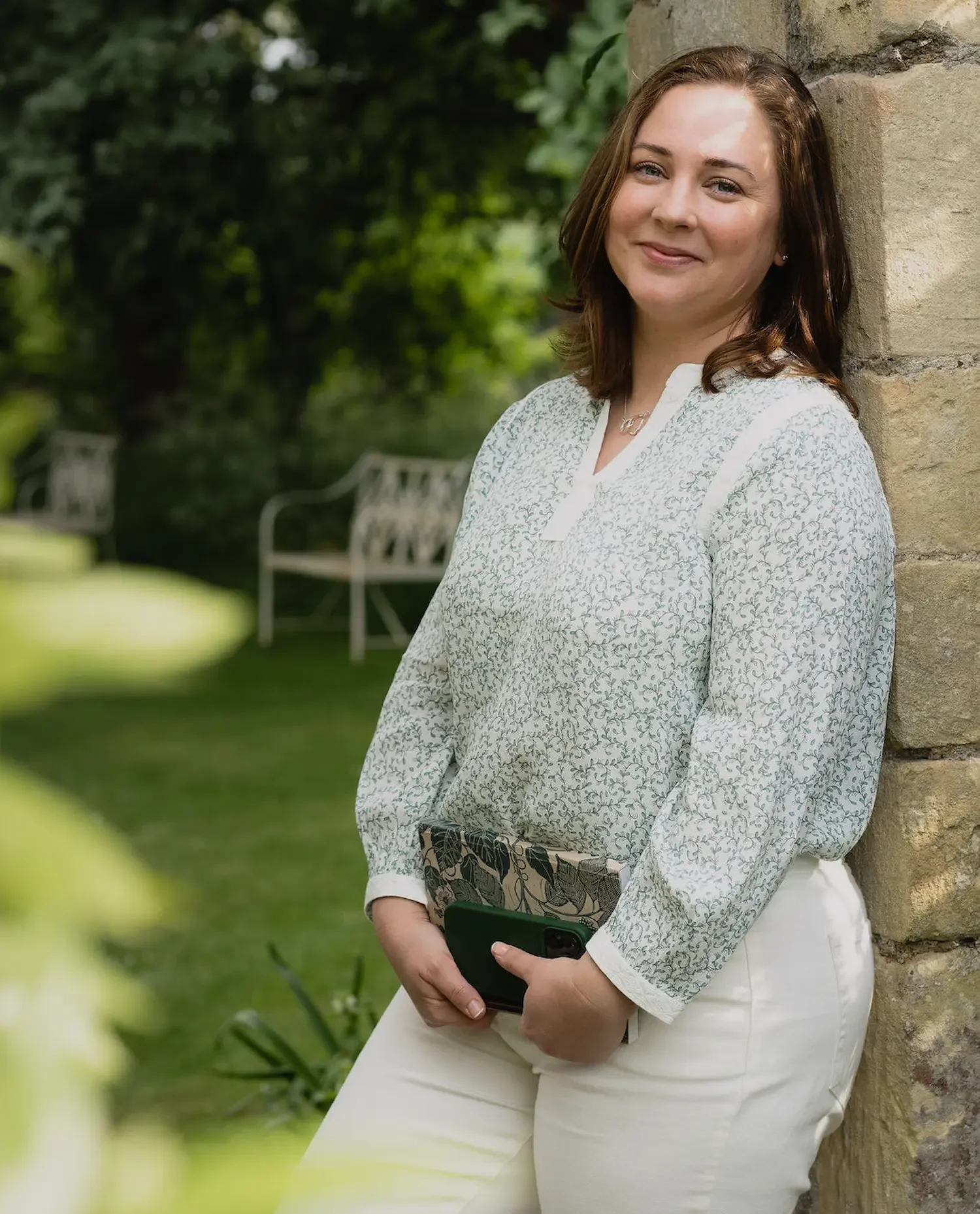 Professional portrait of garden designer Kerianne Fitzpatrick smiling in a green patterned blouse by a stone wall