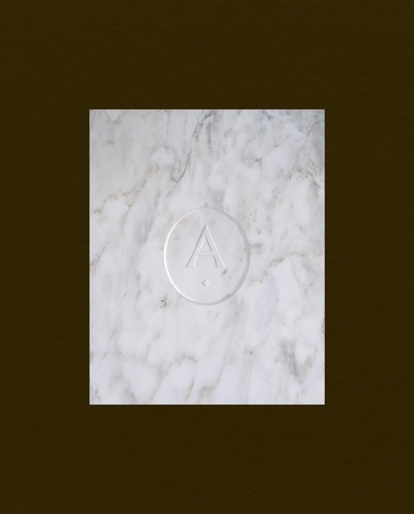 White marble slab with a circular debossed brand seal in the centre featuring the letter A and a small diamond symbol
