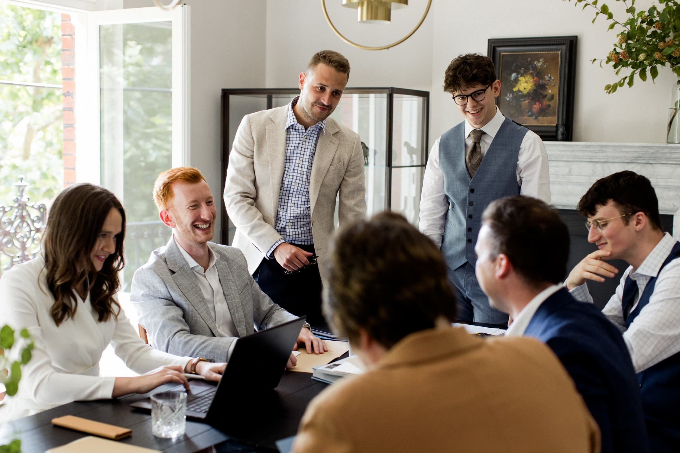 A group of professionals in smart business attire smiling and collaborating around a dark table in a bright modern office