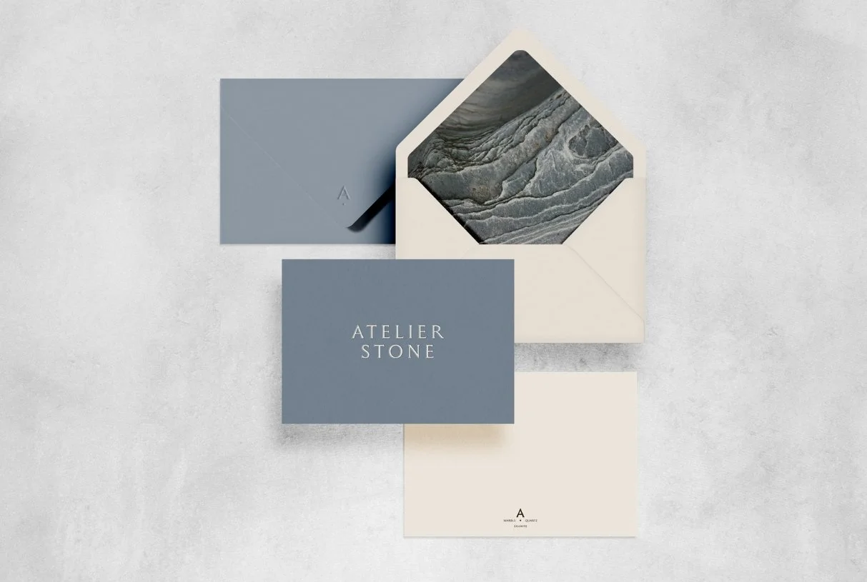 A blue envelope and white envelope with a marble print interior liner featuring a minimalist debossed brand logo