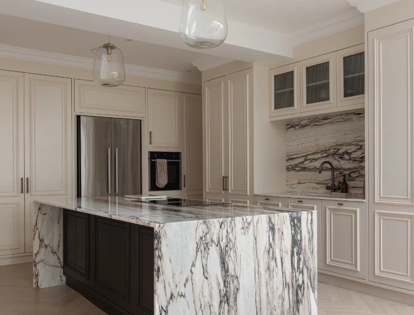 Modern kitchen featuring a large marble island with heavy veining cream cabinetry and stylish glass pendant lighting