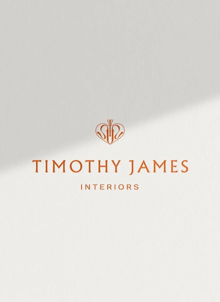 Elegant Timothy James Interiors logo in orange with a decorative crest on a minimalist off-white textured background