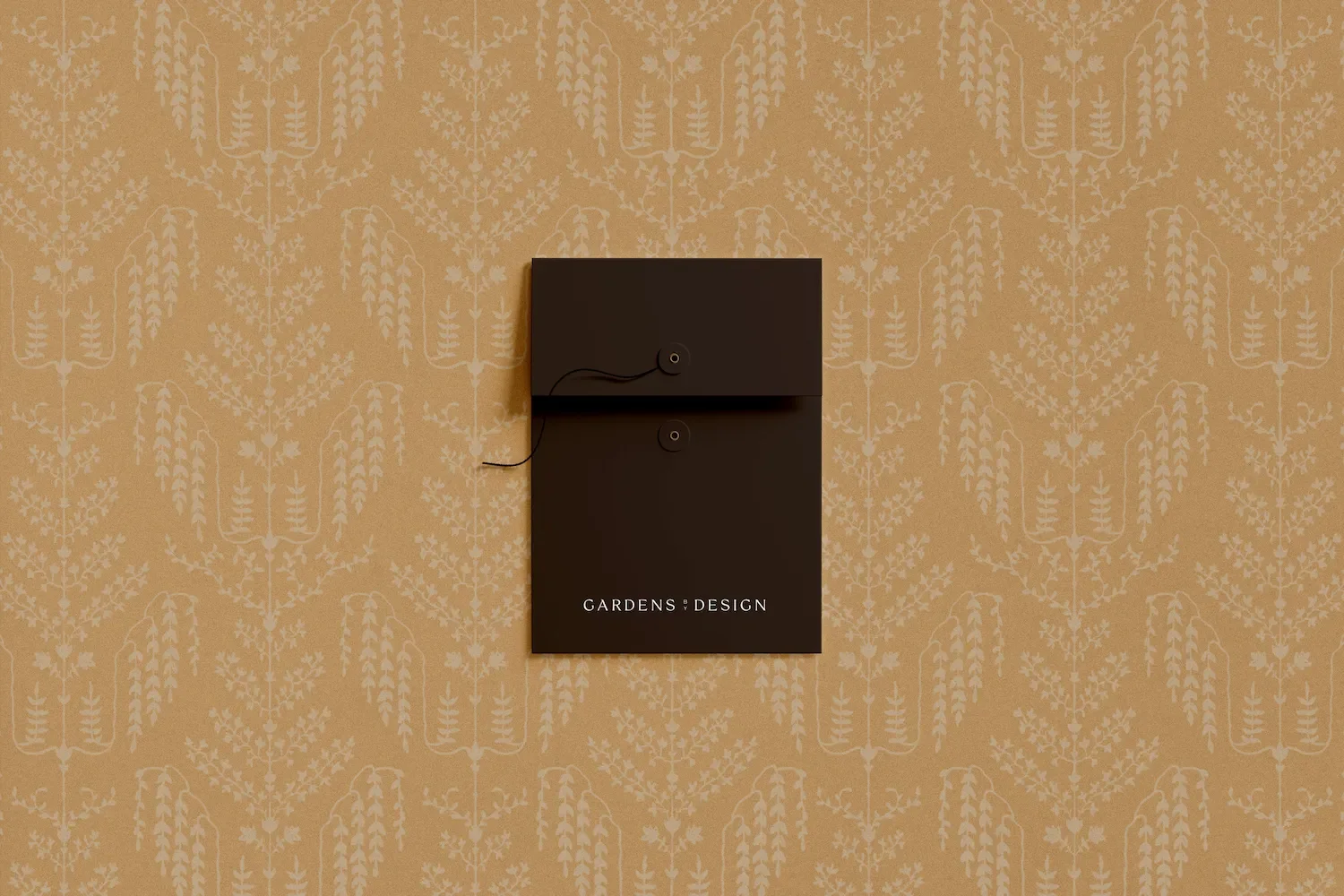 Dark brown string tie envelope branded with the Gardens by Design logo displayed on a patterned botanical background