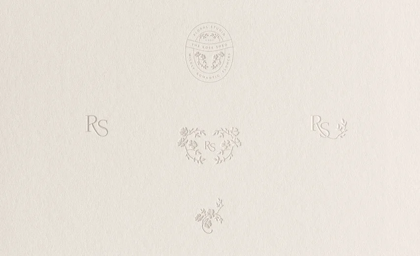 Collection of five different embossed brand marks and floral logos displayed on a clean off-white textured paper surface
