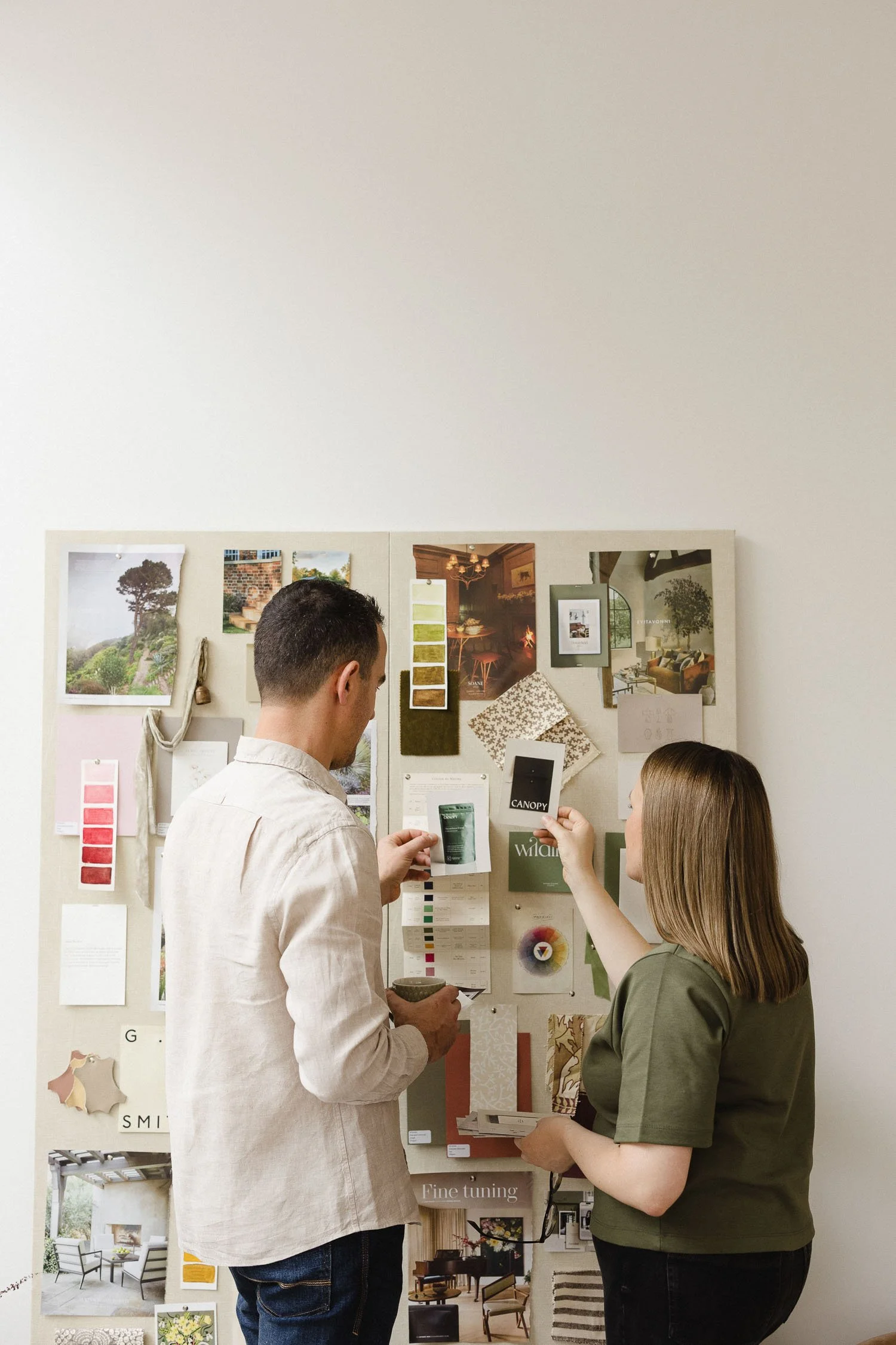 Two designers from Wildings Studio standing at a large pinboard moodboard reviewing garden plus interior design concepts