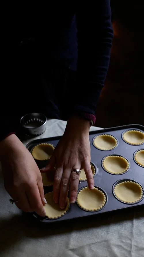 Hands carefully lining a metal cupcake tin with circles of raw fluted pastry to create bases for homemade festive mince pies
