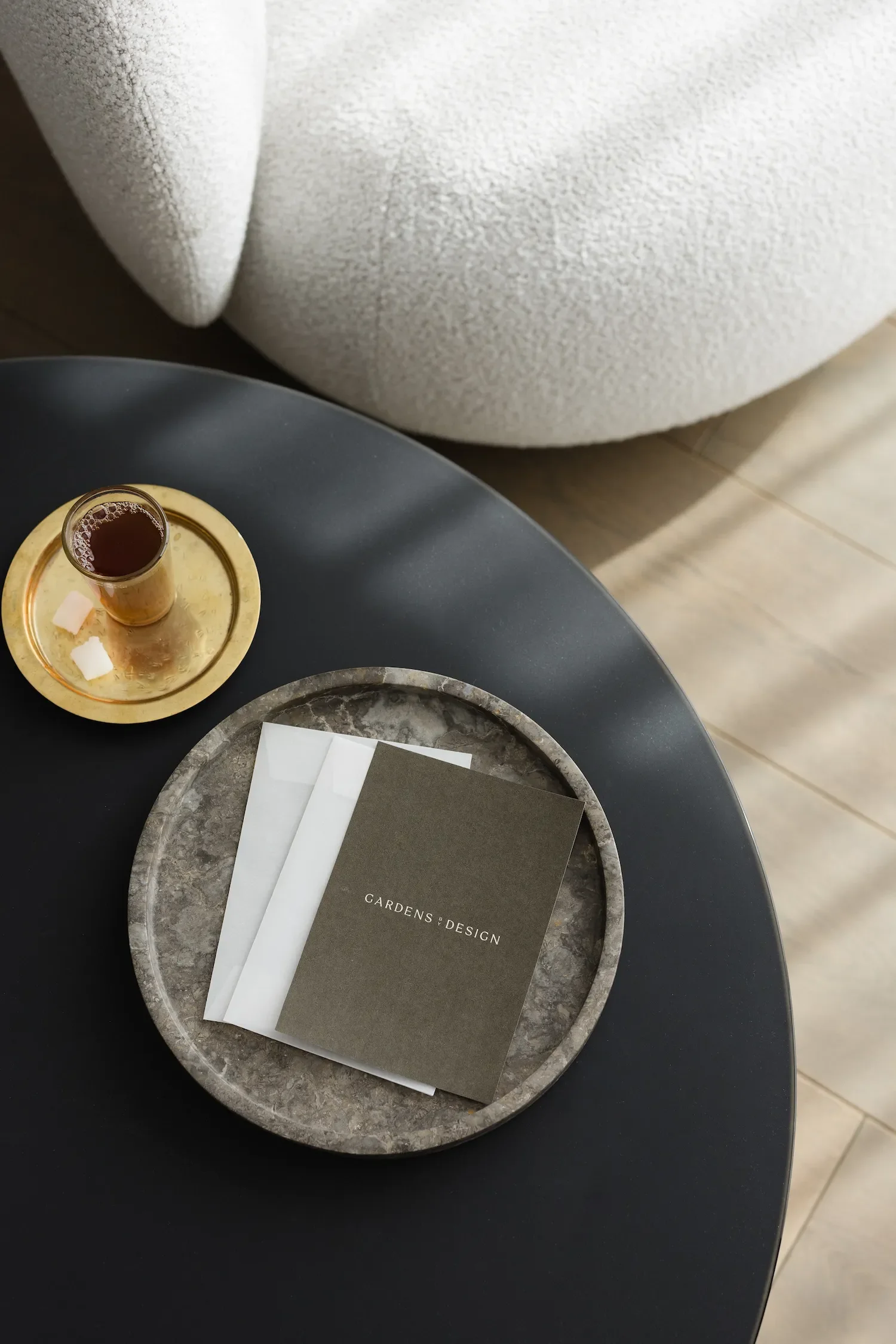 Branded Gardens by Design welcome pack booklet sitting on a marble tray next to a tea glass on a modern coffee table