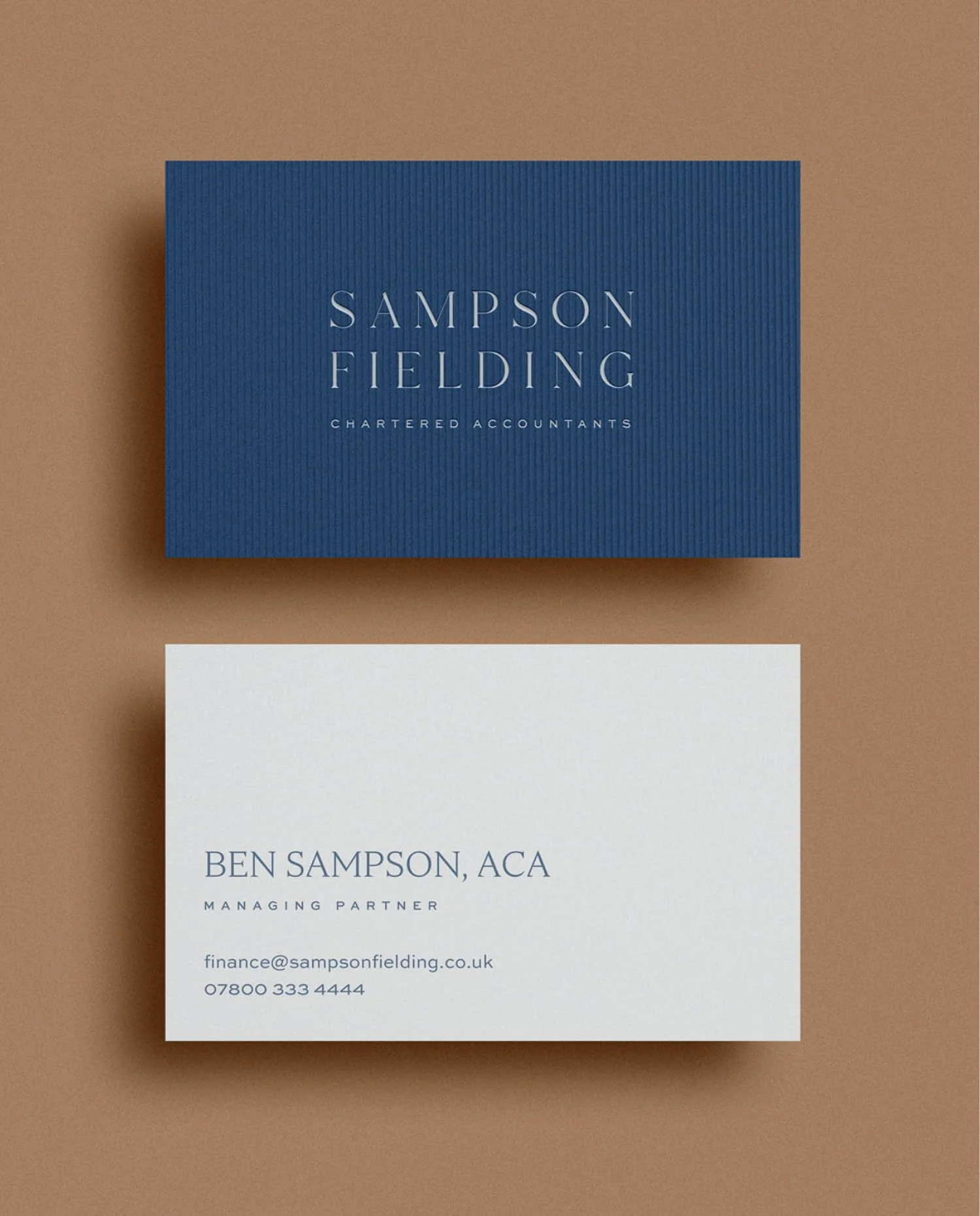 Front and back of Sampson Fielding business cards in navy blue and white with elegant typography and managing partner info