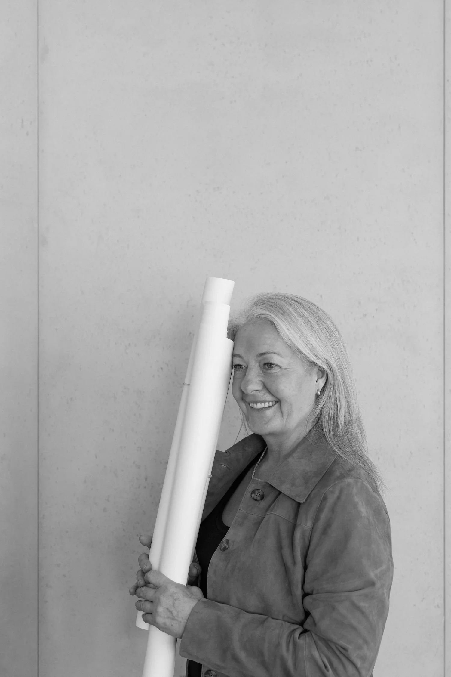 Black and white portrait of Tanja Boehm smiling while holding rolled up architectural garden plans against a neutral wall