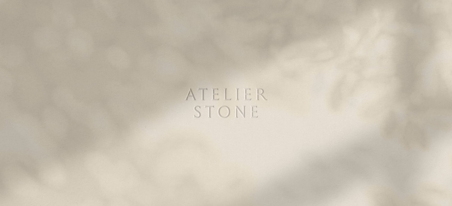 The words Atelier Stone debossed in a minimalist serif font on a light cream textured background with soft leaf shadows