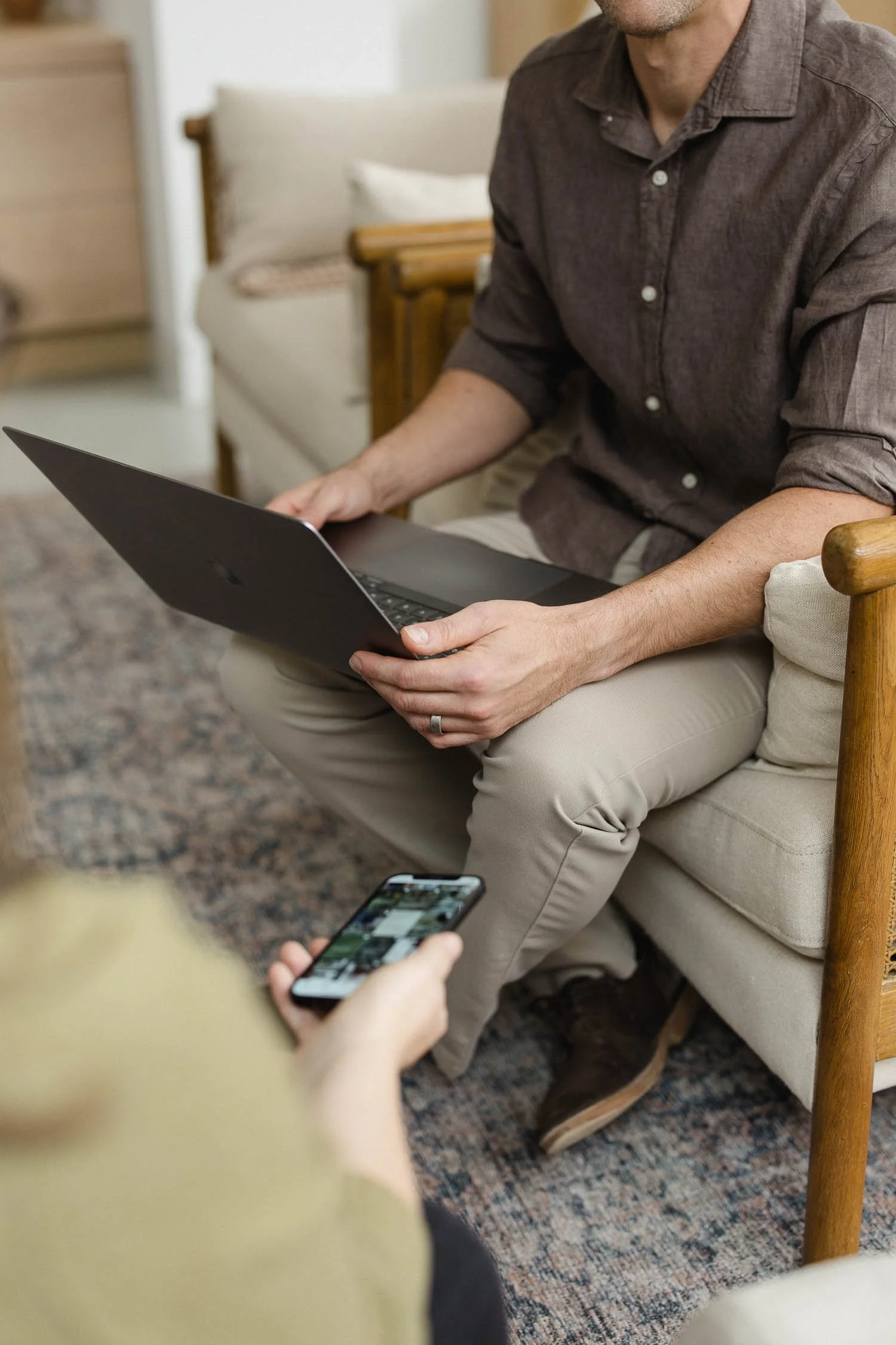 Professional designer holding a laptop while another person shows a website layout on a mobile phone during a studio meeting